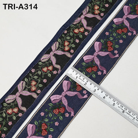 a close-up view of a decorative fabric with a floral pattern and pink bows. A ruler is placed on the fabric, indicating its size.