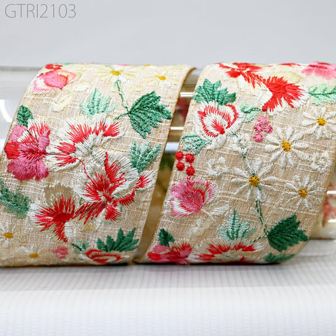 a close-up view of a decorative fabric with a floral pattern, featuring red, green, and white flowers and leaves. The fabric appears to be a ribbon or a piece of cloth with a similar design.