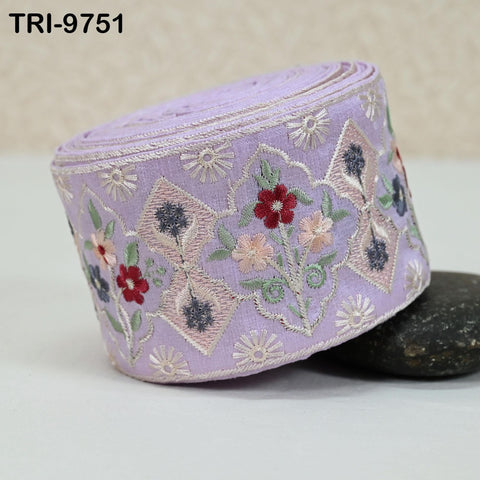 A close-up image of a decorative purple fabric with floral embroidery, resting on a black rock.