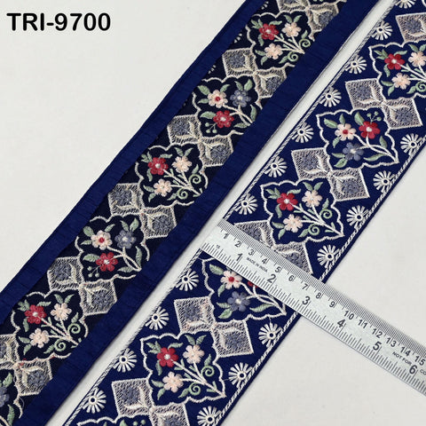 two pieces of blue fabric with intricate floral embroidery patterns. A ruler is placed on the fabric, indicating the size of the fabric pieces.