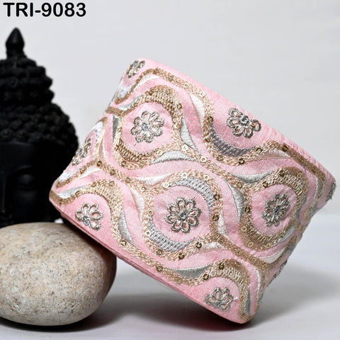 a pink and gold embroidered piece of clothing, possibly a cuff or sleeve, placed on a white surface next to a black Buddha statue and a gray rock.