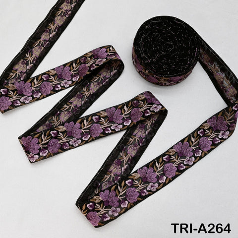 a spool of black and purple embroidered ribbon, along with a piece of the same ribbon, arranged on a white background.