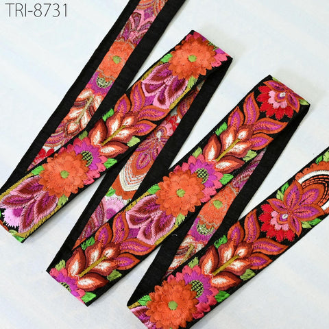 a collection of colorful, intricately embroidered fabric pieces, including a black and pink floral pattern, a red and orange floral pattern, and a pink and orange floral pattern. The fabric appears to be a decorative textile, possibly used for clothing or home decor.