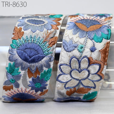 two decorative fabric pieces with intricate floral embroidery in shades of blue, green, and brown. The pieces are arranged side by side, showcasing the detailed craftsmanship of the embroidery.