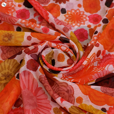 a close-up view of a colorful, printed fabric with a floral pattern. The fabric appears to be made of a soft, light-colored material, possibly cotton or linen. The pattern consists of various flowers and leaves in shades of orange, red, and yellow, creating a vibrant and lively visual effect.