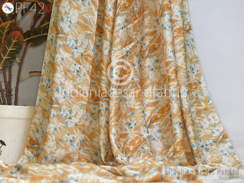 a fabric with a floral pattern in shades of orange and white, hanging on a wall. There is a potted plant in the background, adding a natural element to the scene.