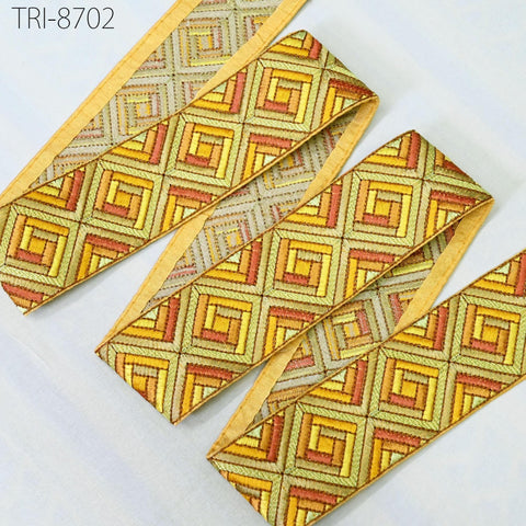 a collection of decorative fabric pieces with a geometric pattern in shades of yellow, orange, and green. The fabric appears to be made of a shiny, metallic material and is arranged in a way that suggests it is part of a larger design or collection.