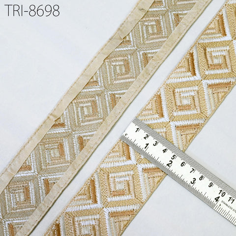 two pieces of beige and gold embroidered fabric, with a ruler placed between them to measure their dimensions.