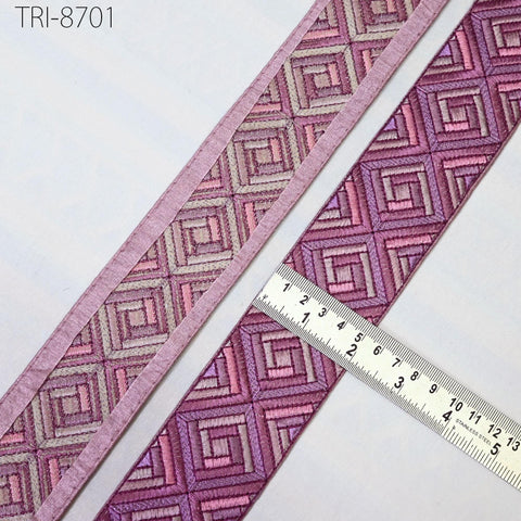 a close-up view of a decorative fabric with a geometric pattern in shades of pink and purple. A ruler is placed next to the fabric, indicating its size or dimensions.