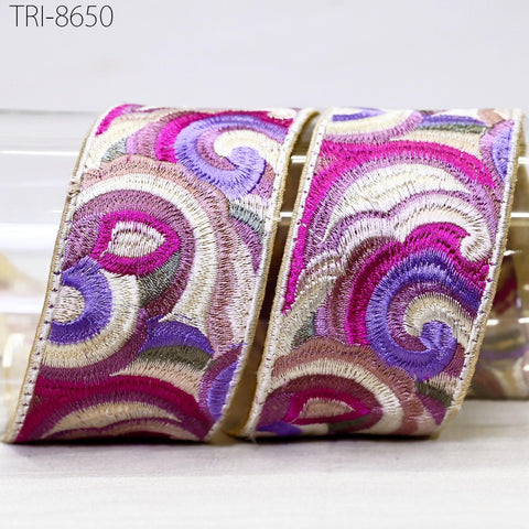a close-up view of a decorative ribbon with a swirling pattern of pink, purple, and white colors. The ribbon appears to be made of fabric and is displayed on a white surface.