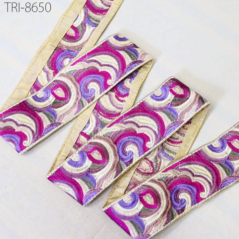 a decorative fabric with a swirling pattern in shades of pink, purple, and white. The fabric appears to be a decorative trim or ribbon, with a gold-colored border.
