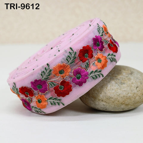 A pink fabric with a floral embroidered design, including red, orange, and purple flowers, is placed on a white surface next to a rock.