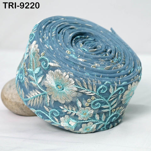 A close-up image of a blue and white floral embroidered fabric, with a textured and rolled appearance.