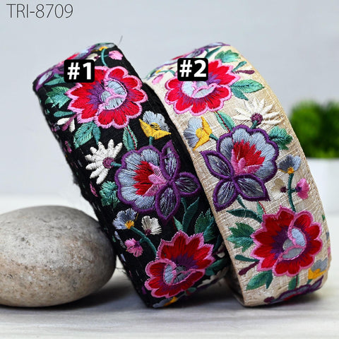 two colorful, floral-patterned headbands with embroidered flowers and leaves, placed on a surface next to a rock.