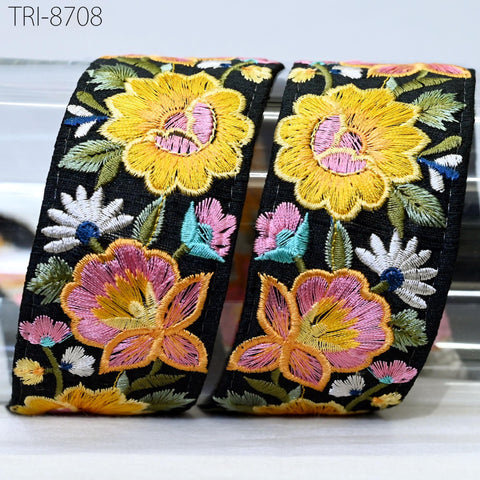 two black fabric pieces with a vibrant floral embroidered design on them. The design includes yellow and pink flowers, along with green leaves and other colorful elements. The fabric pieces appear to be made of a shiny material, possibly silk or satin, and are displayed against a white background.