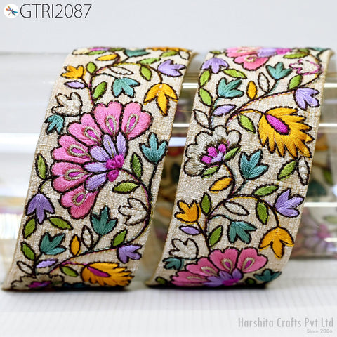 a decorative fabric with a floral pattern in various colors, including pink, yellow, green, and purple. The fabric appears to be a ribbon or textile with intricate embroidered designs.