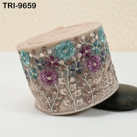 a decorative fabric with a floral pattern, including various shades of green, purple, and white flowers and leaves. The fabric is rolled up and placed on a surface, with a rock visible underneath it.