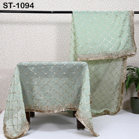 a pair of green and gold patterned fabric pieces, including a tablecloth and a shawl, displayed on a white surface.