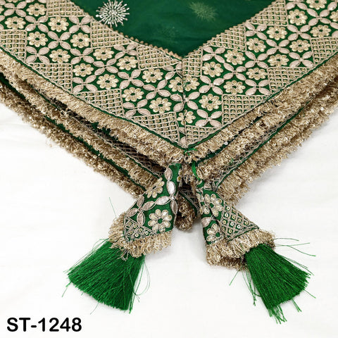 a close-up view of a decorative fabric with intricate floral patterns and tassels in shades of green and gold.