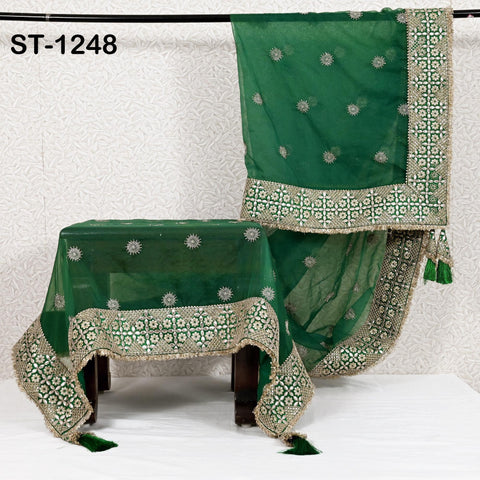 a green and gold embroidered tablecloth with a floral pattern, hanging on a rack.