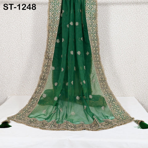 a green and gold embroidered fabric draped over a white surface, with a gold border and tassels at the bottom.