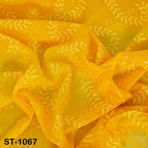 The image is a close-up view of a fabric with a yellow floral pattern. The fabric appears to be made of a soft, flowing material and has a shiny, sequined texture. The pattern consists of white leaves and flowers, creating a visually appealing and intricate design. The image does not contain any text or other objects, and the focus is solely on the fabric and its design.