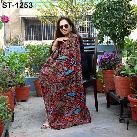 A woman wearing a colorful shawl is posing in a garden surrounded by potted plants.