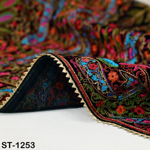 a close-up view of a colorful, intricately embroidered fabric with a paisley pattern. The fabric has a black border and a vibrant array of colors, including red, green, blue, and orange. The image is a close-up of the fabric, showcasing its detailed embroidery and the intricate design of the paisley pattern.