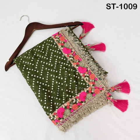 A green and pink embroidered shawl with a floral pattern and fringe tassels is displayed on a wooden hanger.