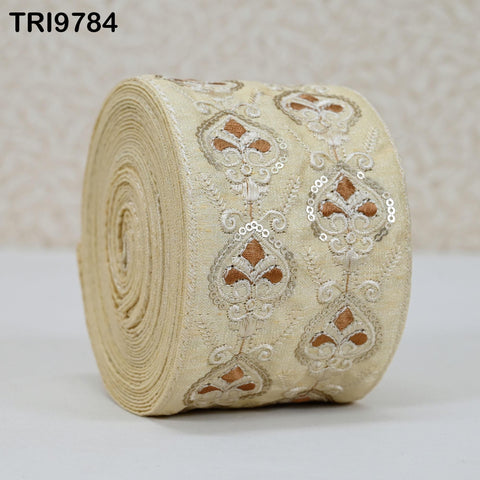 A roll of beige fabric with intricate gold and white embroidered designs.