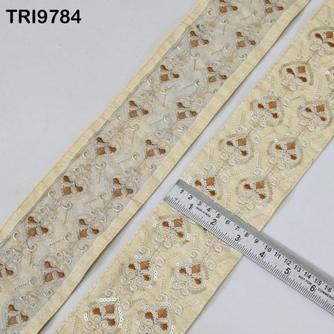 two pieces of fabric with a repeating pattern of gold and white designs, and a ruler is placed on top of one of the pieces to measure its length.