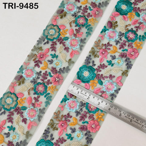 two pieces of fabric with a floral embroidered design, featuring a variety of colorful flowers and leaves. A ruler is placed on top of the fabric, likely for size comparison or measurement purposes.