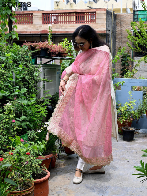 A woman in a pink and white dress stands in a garden surrounded by potted plants.