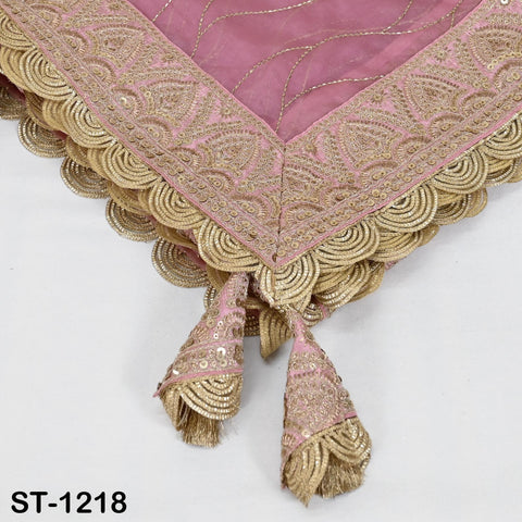 a close-up view of a decorative fabric with intricate gold embroidery and a pink background. The fabric has a scalloped edge and tassels on the ends, adding an elegant touch to the design.