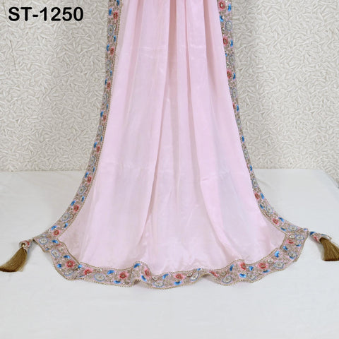 A pink fabric with a decorative border and tassels, displayed on a white surface against a patterned background.