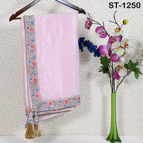 a pink fabric with a decorative border, hanging on a wooden hanger next to a vase of flowers.