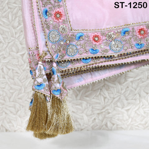A close-up view of a decorative pink fabric with intricate floral embroidery and gold tassels hanging from the edges.