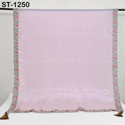 A large, light pink fabric with a decorative border of small, colorful flowers and tassels.
