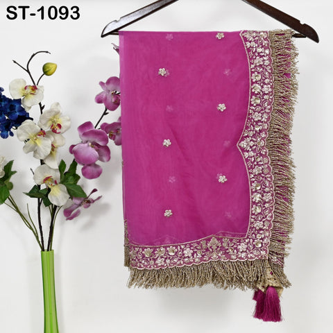 a pink fabric with gold trim, hanging on a wooden hanger next to a vase of flowers.
