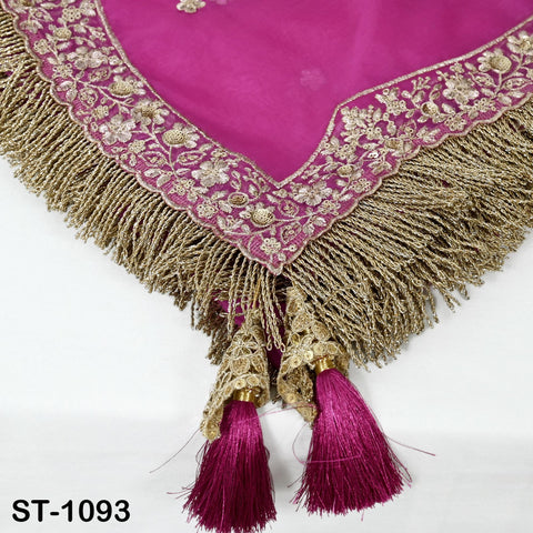 a close-up view of a decorative fabric with a pink background and gold fringe. The fabric has a floral pattern and tassels attached to it.