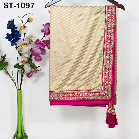 a gold and pink striped saree hanging on a wooden hanger, with a vase of flowers placed next to it on a white wall.