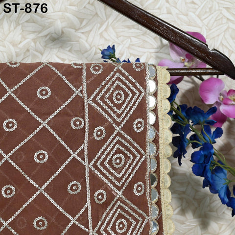 a close-up view of a brown fabric with a diamond pattern, adorned with small white circles and a beige trim. The fabric is hanging on a wooden hanger, and there are purple flowers visible in the background.