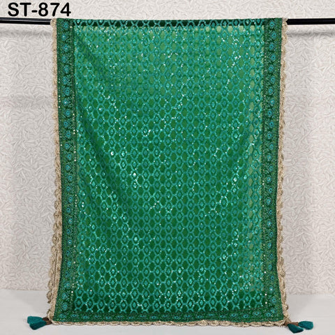 a green sequined fabric with a gold border, hanging on a white wall.