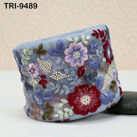 a decorative fabric with a floral pattern, including various types of flowers and leaves. The fabric appears to be a light blue color, and the intricate embroidery work showcases the craftsmanship and attention to detail.
