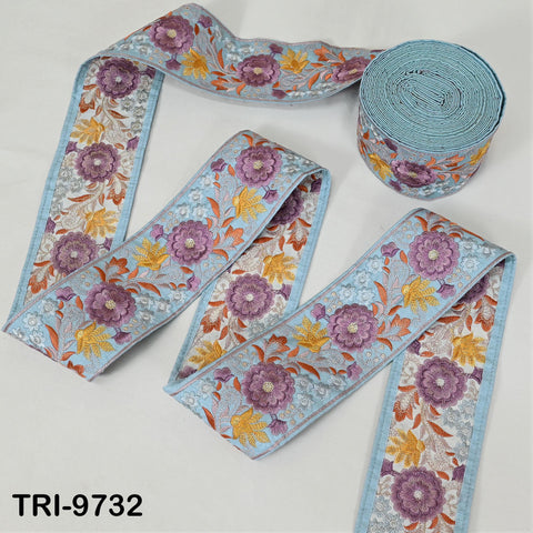 a collection of decorative fabric pieces with floral patterns in shades of blue, purple, and yellow. The pieces are arranged on a white background, with a roll of blue fabric visible in the top right corner.