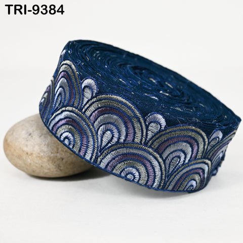 a close-up view of a decorative blue fabric with a repeating pattern of waves or swirls in shades of blue, purple, and white. The fabric appears to be a decorative trim or ribbon, and it is placed on a white surface.