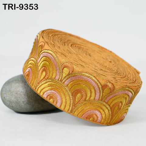 a decorative orange and gold fabric with a repeating pattern of waves or circles, placed on a white surface next to a gray rock.