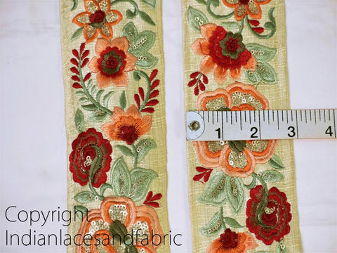 two pieces of fabric with intricate floral embroidery, including red, orange, and green flowers, as well as leaves and other decorative elements. A ruler is placed between the two pieces of fabric to indicate their size.