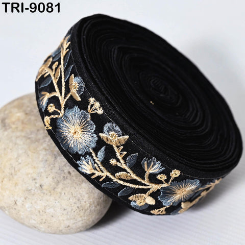 a black fabric with a floral pattern, including blue and gold flowers, and a black circular object with a gold floral pattern.