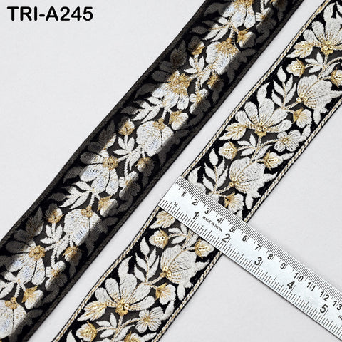 two spools of black and gold embroidered ribbon, with a ruler placed between them to measure the length of the ribbon.
